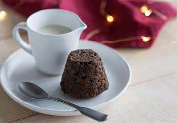 Christmas pudding on a white plate next to a jug of cream.