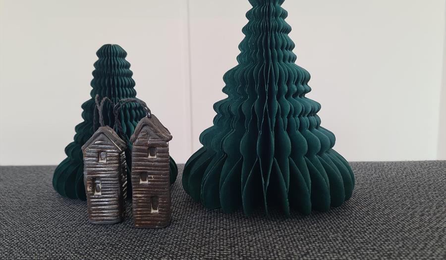 Photograph of paper 3d christmas tree in concertina style. In font is a small model of elongated huts.