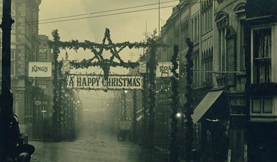 black and white photograph of street scene with tinsel christmas decorations lining the street.