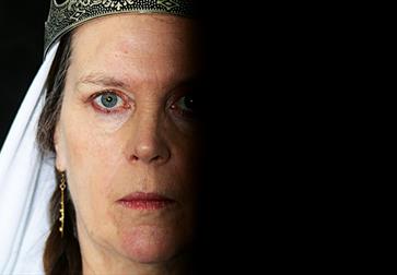 close up portrait of a white woman staring coldly at the camera, one half of face in complete shadow, a crown slightly visible