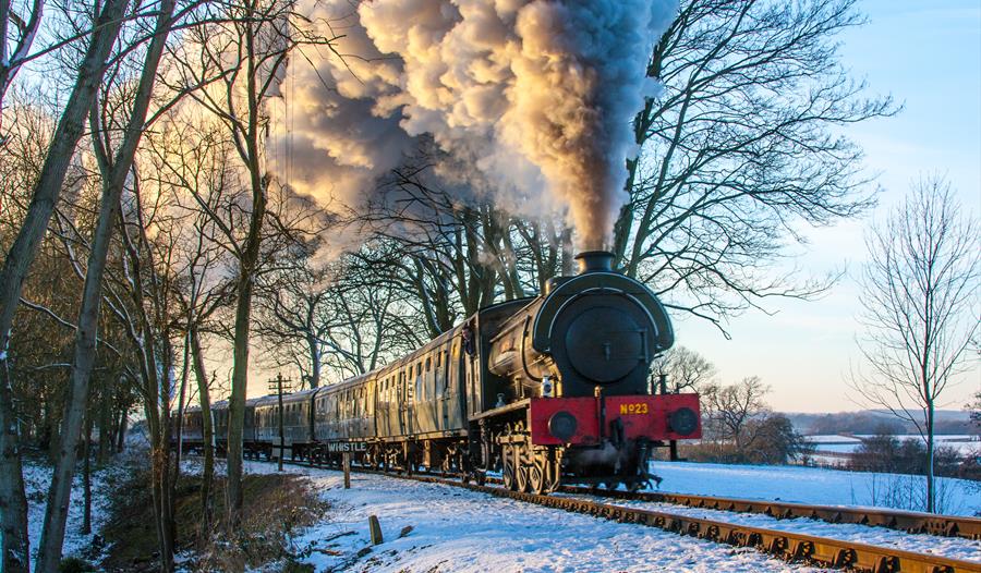 A steam train passing, ground has light snow.