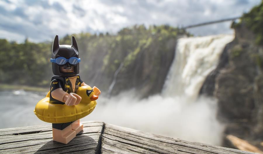 lego batman figure wearing rubber ring on a ledge with a waterfall in the background.