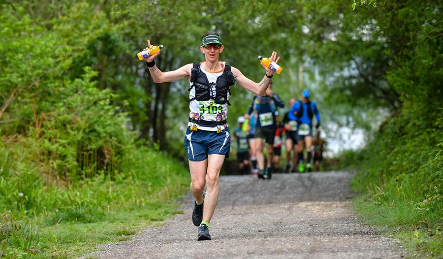 runner on tree lined track holding up hands with drinks bottles