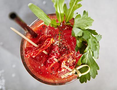 birds eye view of a bloody mary cocktail, red drink with celery leaves as gardnish
