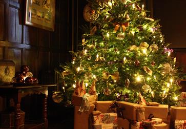 traditional christmas tree aglow with warm lights and brown parcels beneath.