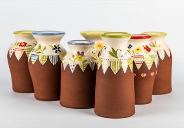 photo shows ceramic pots lined up with terracotta bases and glazed patterned tops.