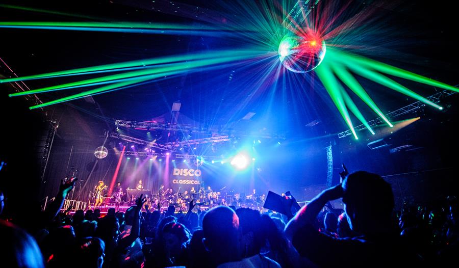 photo showing crowded club night with green lasers and disco ball,