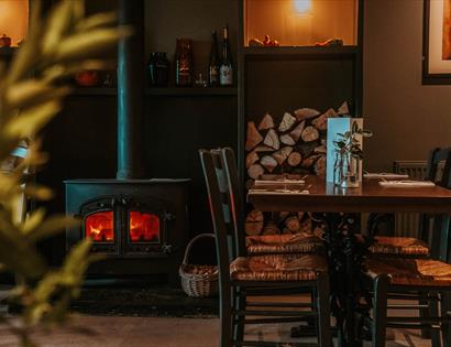 cosy pub interior with table and chairs next to a log burning stove.