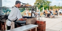 chef working outdoor grill, with customers sat on tables on patio terrace