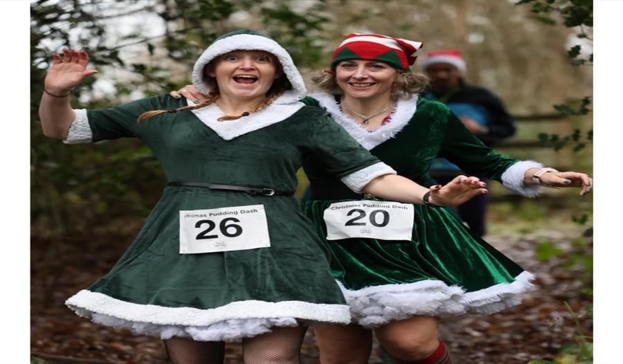 Festive holiday run: two women dressed as Santa jogging together on a forest path. Festive holiday run: two women dressed as Santa jogging together on a forest path.