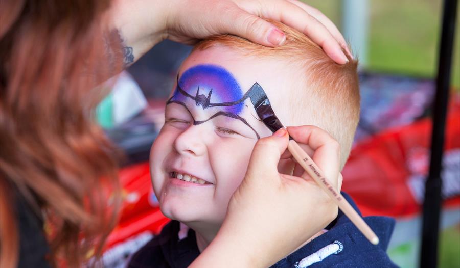 a young boy having his face painted.