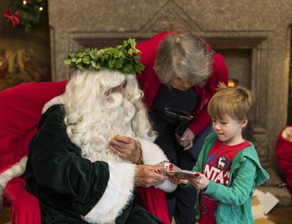 Man with long white hair, long beard and leaf headpiece giving a gift to a small boy.