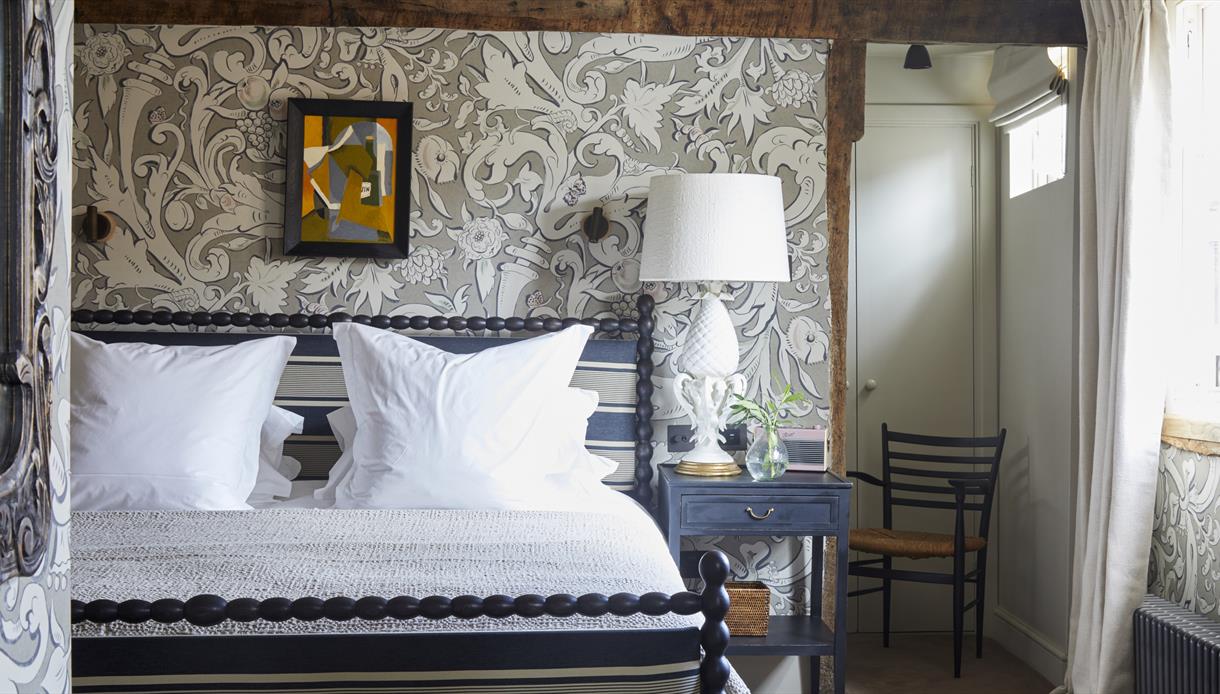 interior view of bedroom shows decorative wallpaper, wooden chair, and deluxe double bed with white sheets