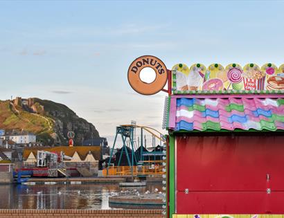 photograph of Hastings, with donut sign and colourful hut in the foreground and hill with funicular railway in the background.