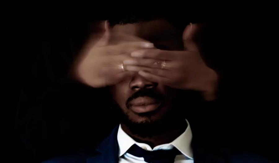 portrait against a black background of black man with a woman's hands covering his eyes.