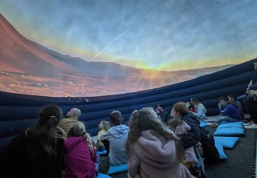 children stat inside a planetarium looking up a bare red planet landscape.