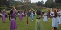 women in dresses holding ribbons around a May pole.
