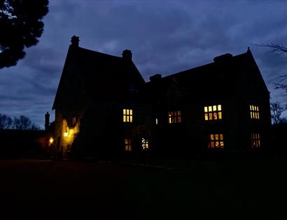 silhouette of a large house at twilight with rooms aglow.