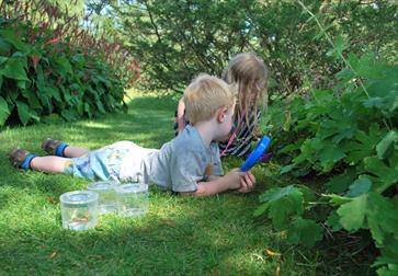 two young children exploring in a garden with pots and a magnifying glass.