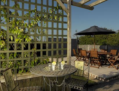 Garden at Stoats Holiday Home shows terrace and tables in sunshine