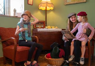 children and mum sat in 50s-style living room wearing hats.