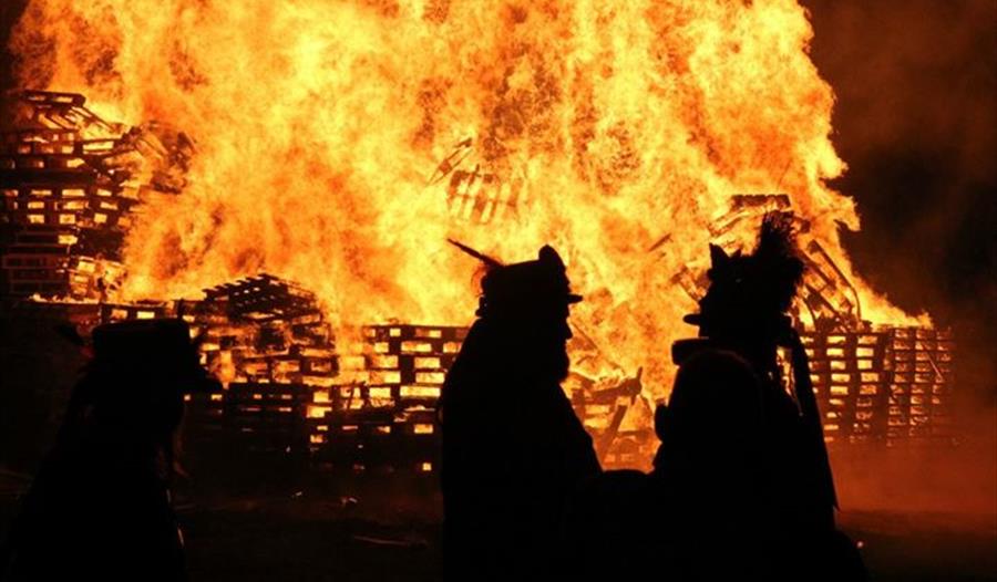huge bonfire fire of pallet crates with two silhouetted figures in the foreground