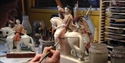 A ceramic piece of a man on a horse holding an eagle. A hand is in the foreground holding a paintbrush to the figurine.