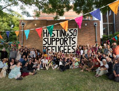 Crowd at Sanctuary Festival surround a large poster that reads 'Hastings supports Refugees'.