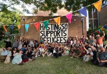 Crowd at Sanctuary Festival surround a large poster that reads 'Hastings supports Refugees'.