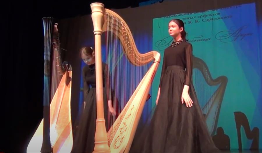 lady on stage in black dress stood next to harp.