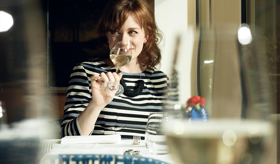 A lady smiling sipping white wine.
