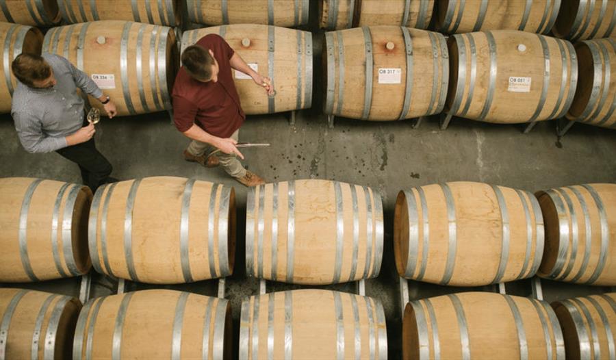 birds eye view of winery with two men walking past rows of barrels.