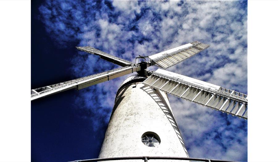 a photograph of a white windmill against a blue sky. Taken from below windmill looking upwards.