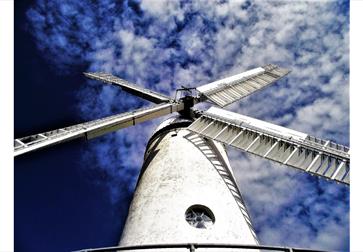 a photograph of a white windmill against a blue sky. Taken from below windmill looking upwards.
