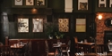Interior view of pub setting with deep dark green panelled walls with artworks displayed.