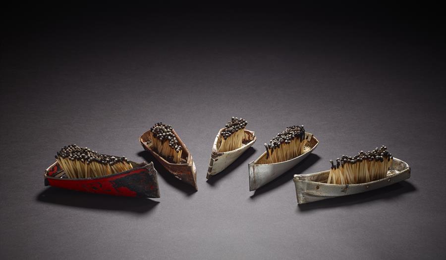 a photograph with five miniature boats with crowds matches standing upright within them, against a plain grey background. a photograph with five miniature boats with crowds matches standing upright within them, against a plain grey background.