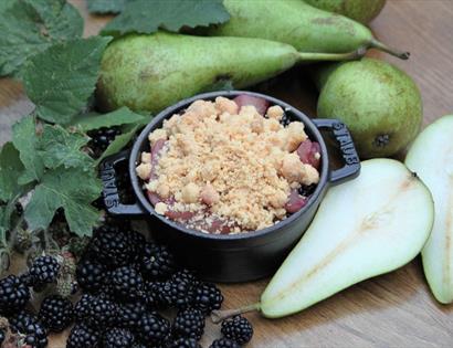 Photograph of small crumble dish with pears and berries surrounding.