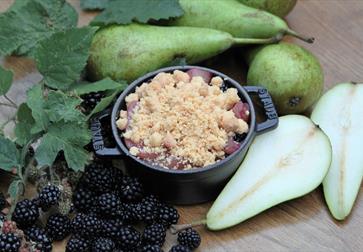 Photograph of small crumble dish with pears and berries surrounding.