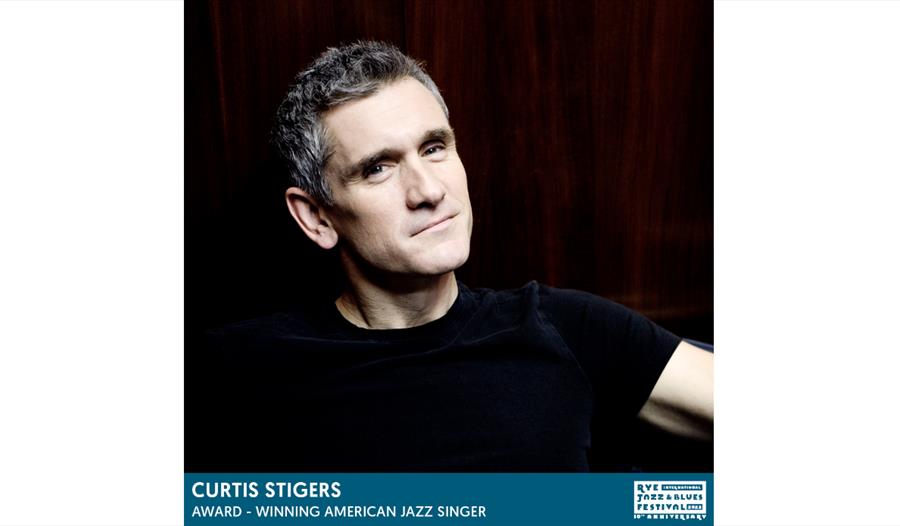 portrait of white man with grey hair wearing black tshirt, text underneath says curtis stigers award winning american jazz singer
