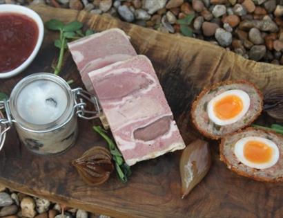 gourmet ham and a scotch egg served on a wooden platter.