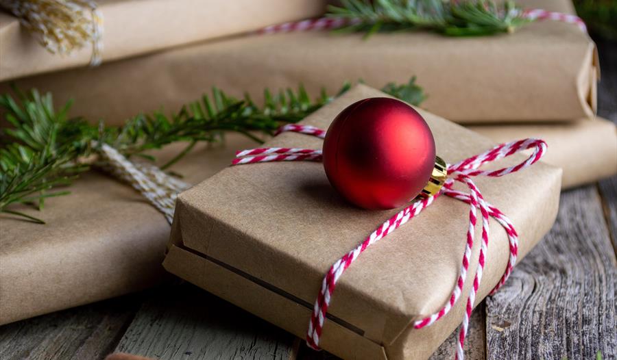 photograph of parcel-wrapped gifts with red bauble and sprigs of christmas tree.