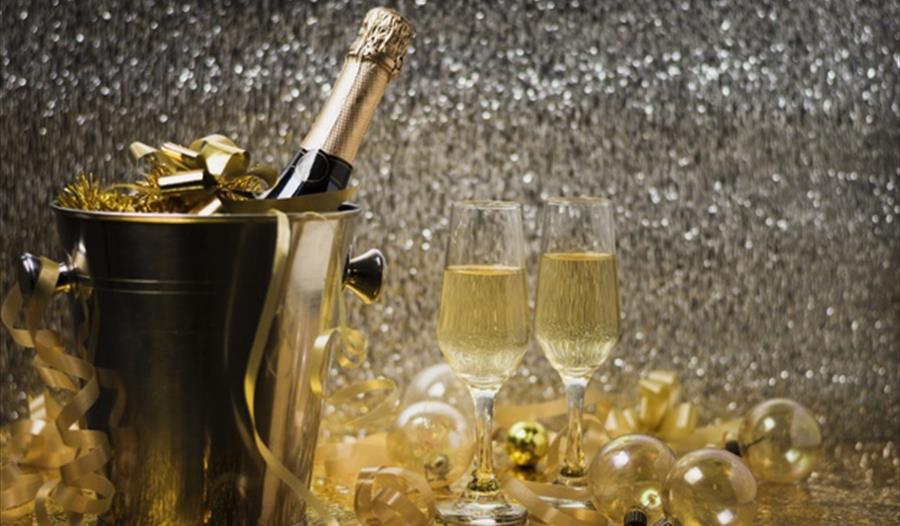 photograph of champagne in ice bucket with two glasses and silver and gold decorations.