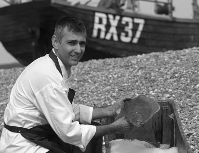 A photograph of a chef on a beach with locally caught fish