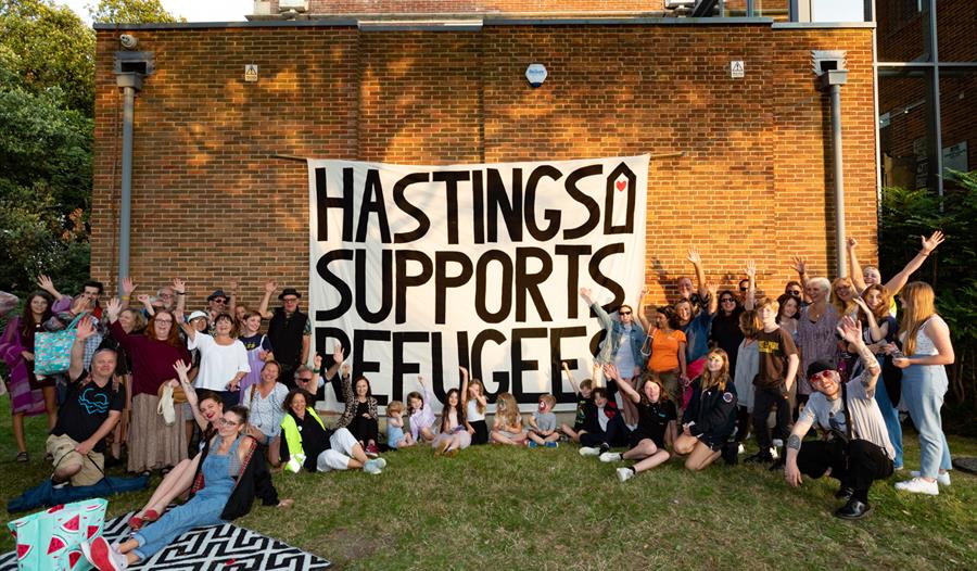 Large banner with Hastings Supports Refugees print pinned against brick wall with crowd around it.