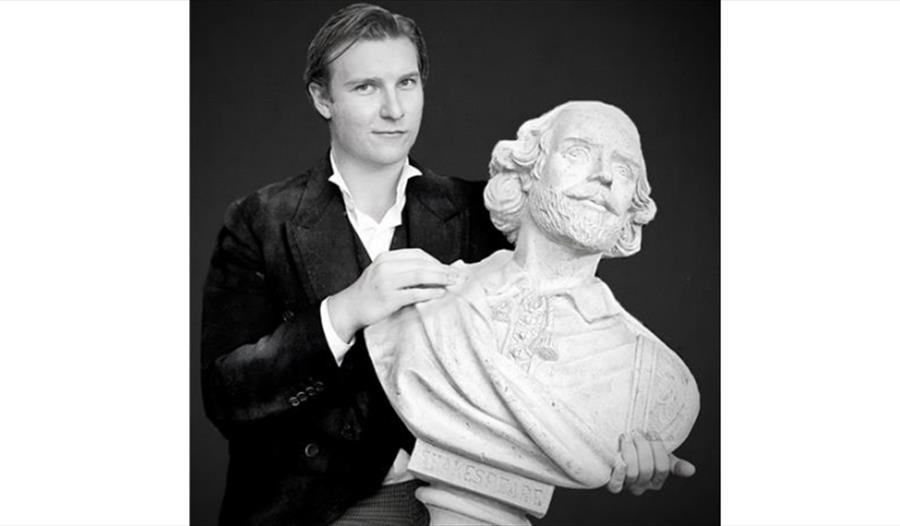 A black and white photograph of a white man holding a bust of Shakespeare.