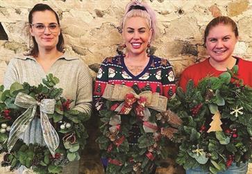 Three women hold up Christmas wreaths.