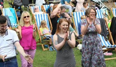 People dance in a park in front of deck chairs.