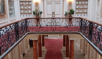 A grand staircase with red carpet inside Croxteth Hall