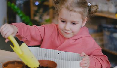 A child wearing a pink jumper holding a yellow shovel digging in mud