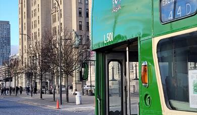 A classic green bus parked outside the Royal Liver Building in Liverpool.
